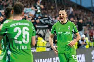 Zwei Fu ballspieler in gr nen Trikots mit wei en Nummern, einer tr gt die Nummer 26, der andere die Nummer 15, im Stadion vor Zuschauern.