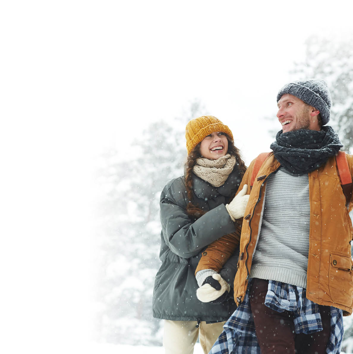 Jolly beautiful young couple in puffy jackets holding hands and laughing while enjoying winter stroll, hiking in forest