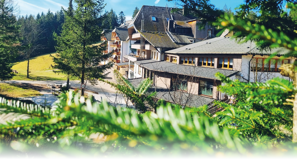 Mehrst ckiges Geb ude mit Satteldach in bewaldeter H gellandschaft bei klarem Himmel   