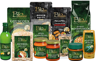 Verschiedene Bio Rinatura Lebensmittelverpackungen und Flaschen mit Produkten wie Couscous, Dinkel gepufft, Power Patty, Falafel, Soja Schnetzel, Zitronensaft, Paprika Cashewkerne, Kidneybohne Tomate, Salatkernmix, Gem sebouillon, Dinkel Bandnudeln und Agavensirup