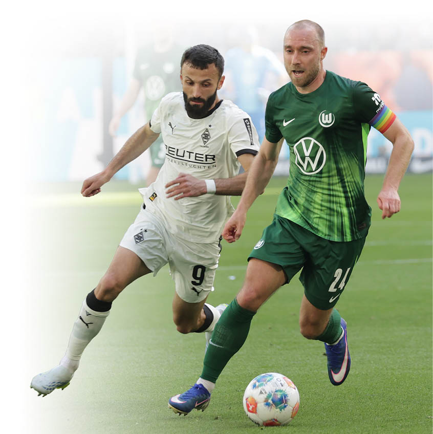 Zwei Fu ballspieler k mpfen w hrend eines Bundesligaspiels um den Ball. Ein Spieler im gr nen Trikot des VfL Wolfsburg sprintet mit dem Ball nach vorne, dicht verfolgt von einem Spieler in wei em Trikot von Borussia M nchengladbach. Im Hintergrund sind weitere Spieler und Zuschauer im Stadion unscharf zu sehen.