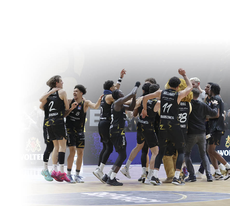Eine Gruppe von Erwachsenen in schwarzen Basketballtrikots feiert gemeinsam auf einem Basketballfeld vor Zuschauern. Beschreibung von KI generiert
