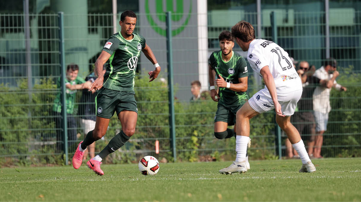 Drei Personen spielen auf einem Fu ballfeld, zwei tragen gr ne Trikots und eine tr gt ein wei es Trikot, w hrend sie sich auf den Ball konzentrieren. Beschreibung von KI generiert
