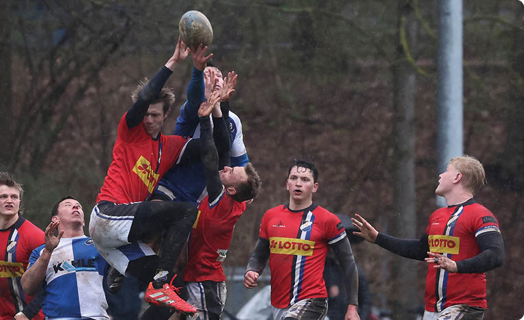 Drei Personen in Sportkleidung sind in einer dynamischen Szene bei einem Spiel im Freien zu sehen, wobei eine Person hochgehoben wird und die anderen aufmerksam zuschauen. Beschreibung von KI generiert