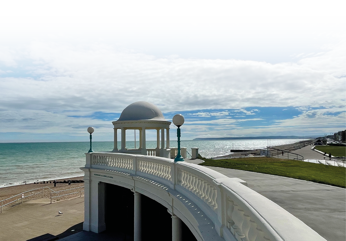 Eine wei e, elegante Strandpromenade mit einer kleinen Kuppelterrasse erstreckt sich entlang eines ruhigen Meeres unter einem teilweise bew lkten Himmel. Beschreibung von KI generiert