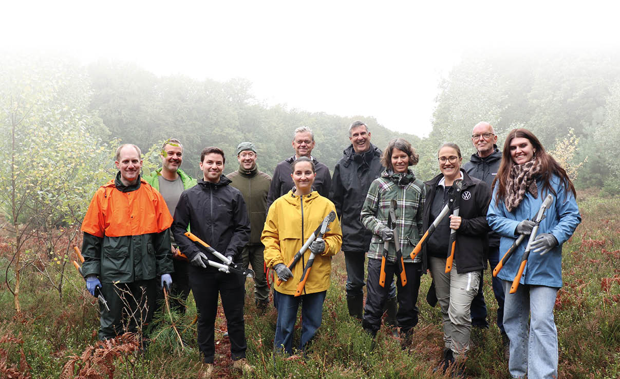 Eine Gruppe von Menschen in Outdoor-Bekleidung steht auf einer Wiese mit Werkzeugen in der Hand, umgeben von B umen und Nebel im Hintergrund. Beschreibung von KI generiert