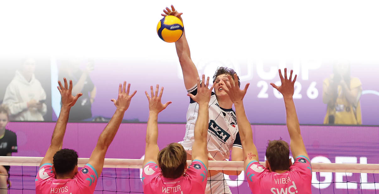 Ein Spieler in wei er Sportkleidung springt hoch und schl gt einen Volleyball ber ein Netz, w hrend drei Spieler in pinken Trikots mit erhobenen Armen versuchen, den Ball zu blockieren.  Beschreibung von KI generiert