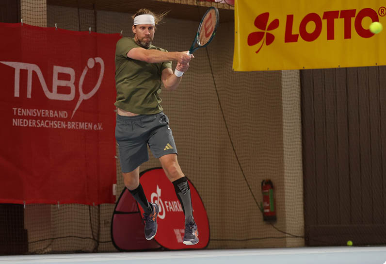 Eine Person tr gt graue Shorts mit einem goldenen Adidas-Logo und schwarze Sportsocken und befindet sich in einer Sporthalle mit Netz und Feuerl scher im Hintergrund. Beschreibung von KI generiert