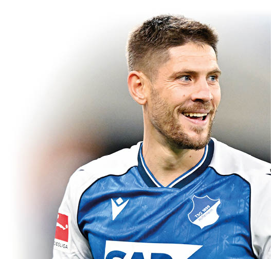 Eine Person mit kurzem Haar tr gt ein blau-wei es Fu balltrikot und l chelt w hrend eines Spiels. Beschreibung von KI generiert